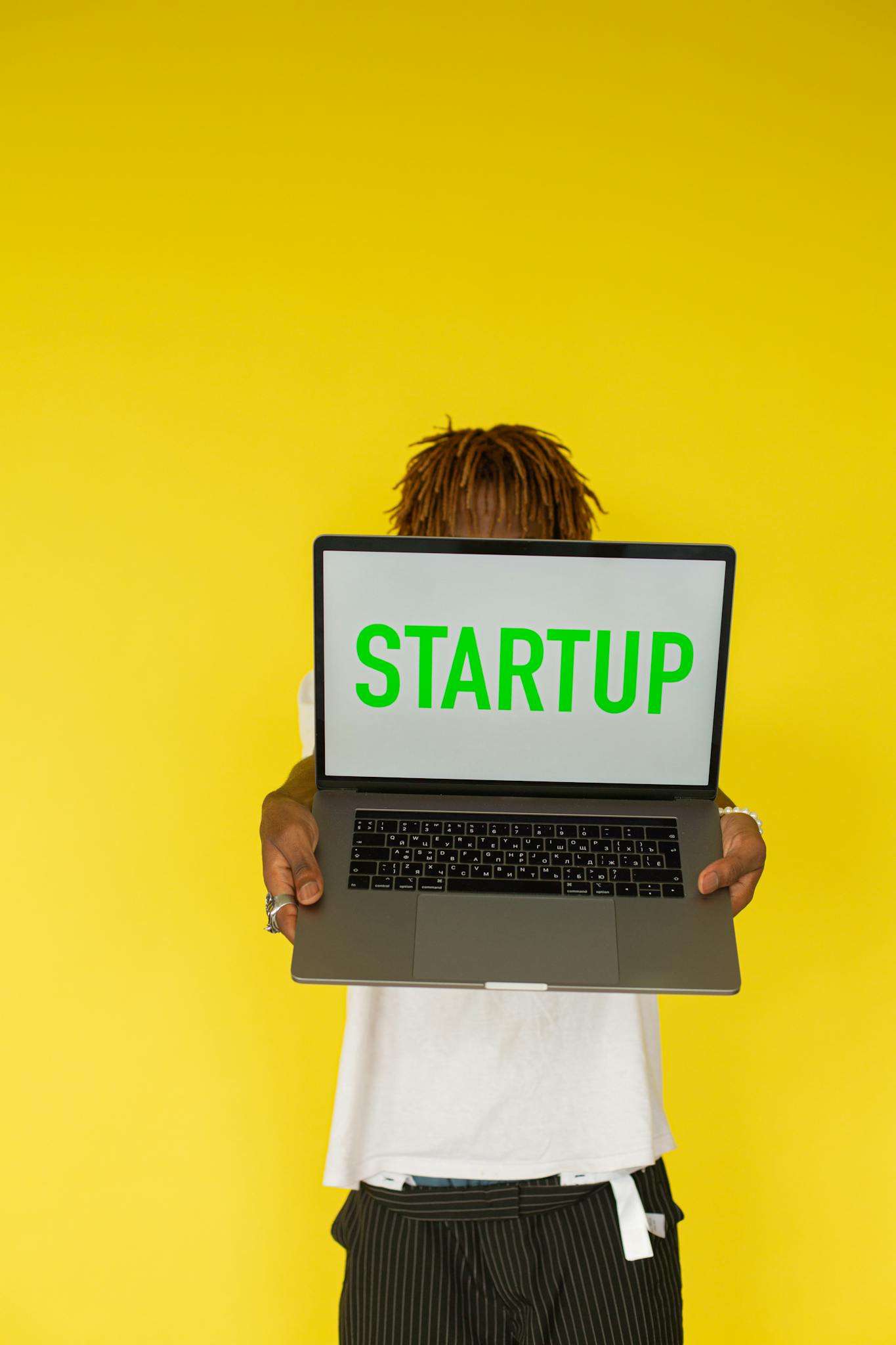Person holding a laptop with 'STARTUP' text against a bright yellow background, symbolizing innovation.